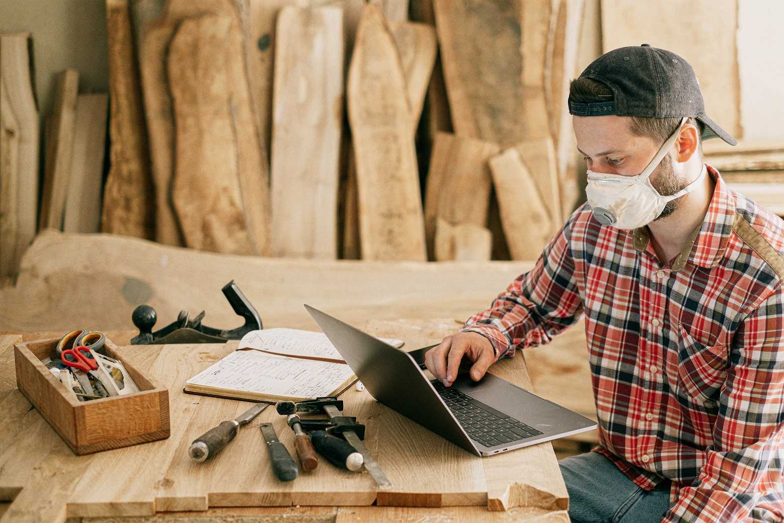 Joinery worker in a protective mask works on a laptop